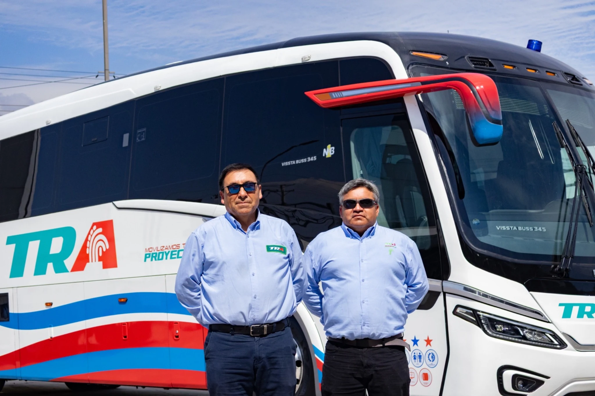 Dos colaboradores TRA junto a un bus de la empresa durante la entrega de unidades